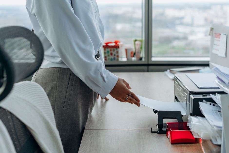 A frustrated small business owner looking at an offline office printer, with a laptop showing troubleshooting steps.